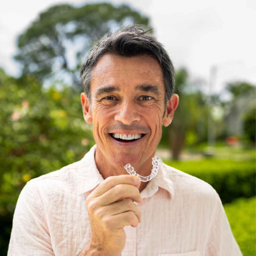 man smiling and holding an invisible day mouth guard for teeth protection